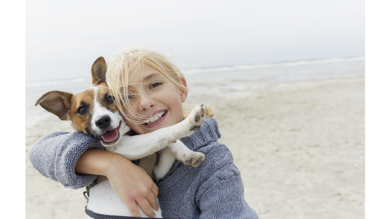 Happy girl hugging dog on the beach, portrait