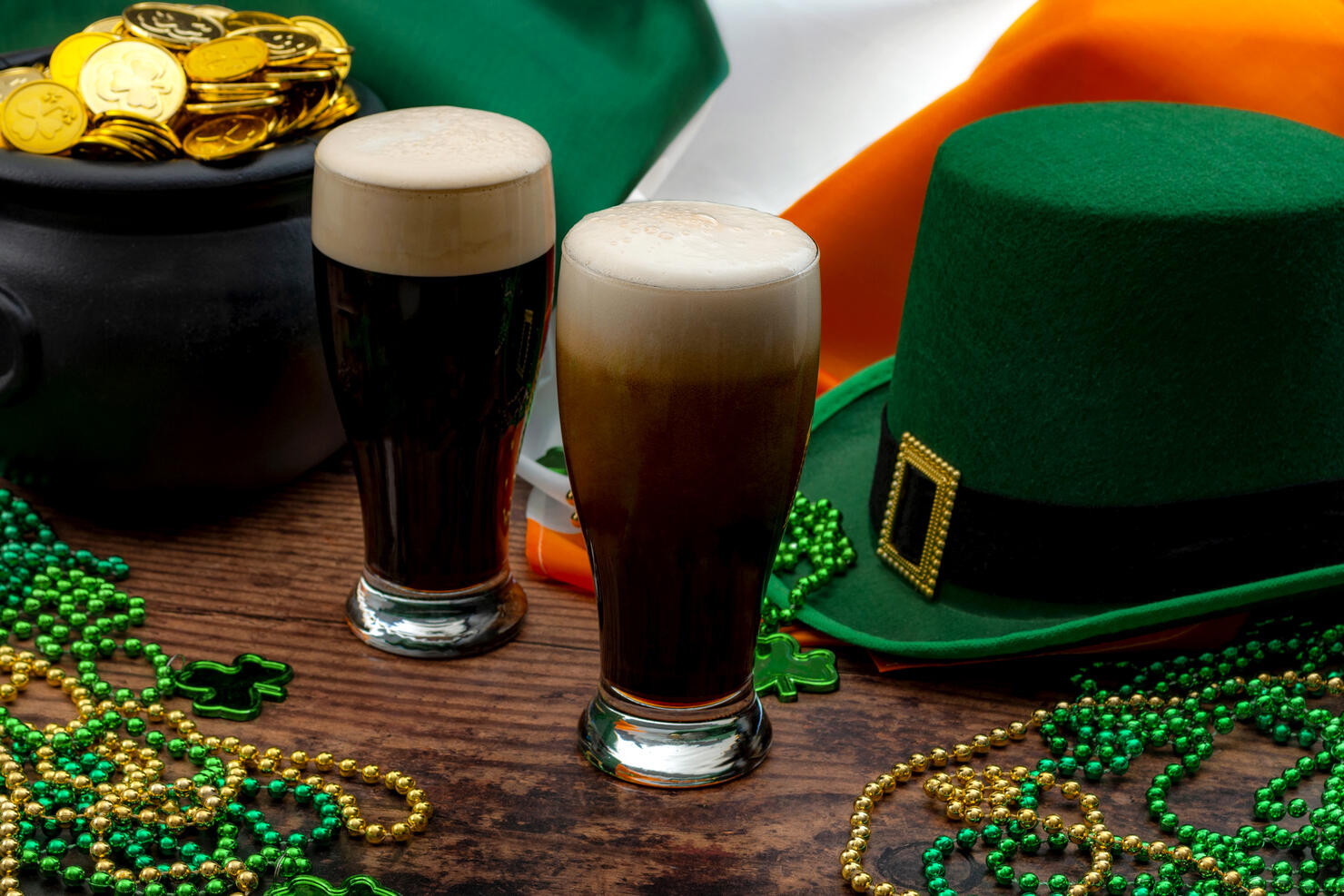 St Patrick's day party and Irish celebration of patron saint concept theme with frothy glasses of dry stout, green hat with a buckle, a pot of gold, the flag of Ireland and beads with shamrock in a pub
