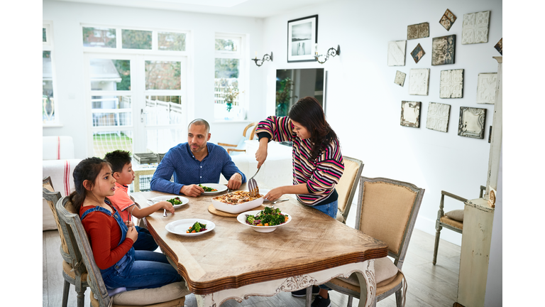 Mid adult woman serving family dinner to husband and children