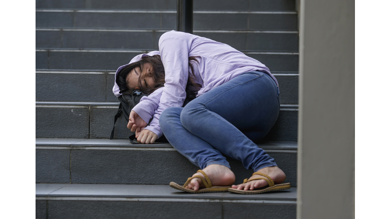 dramatic portrait of young depressed and intoxicated Asian student woman or teenager girl sitting on street staircase drunk or high on drugs suffering addiction problem and anxiety