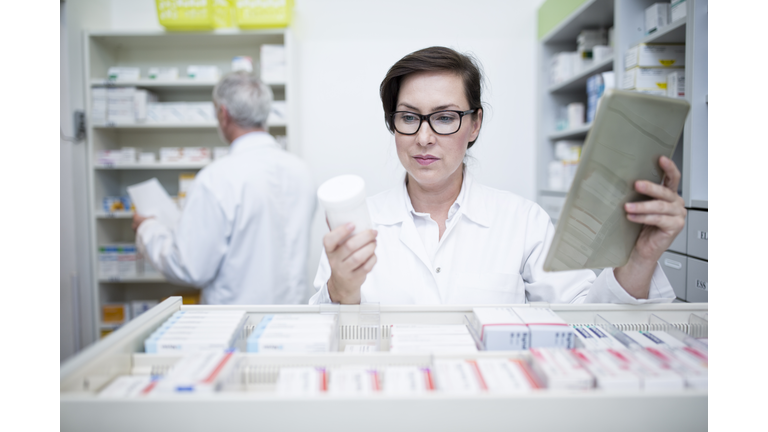 Pharmacist with tablet and medicine at cabinet in pharmacy