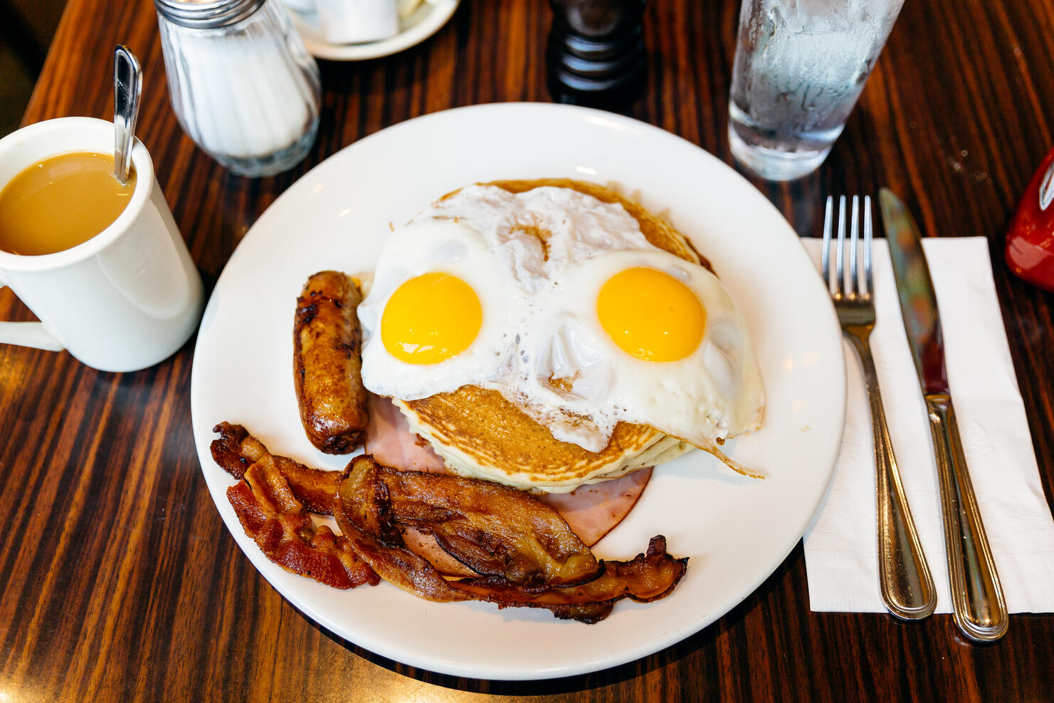 Traditional American breakfast with pancakes, fried eggs, bacon, sausage and ham served in a diner