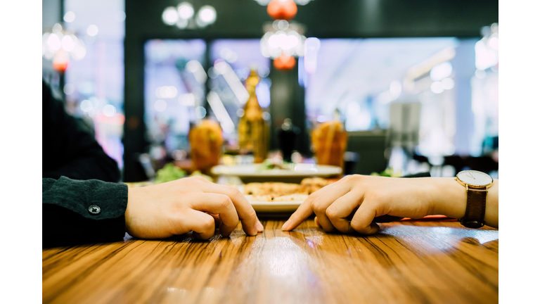 Couple going on a first date and attempting to hold hands during a dinner date at a restaurant