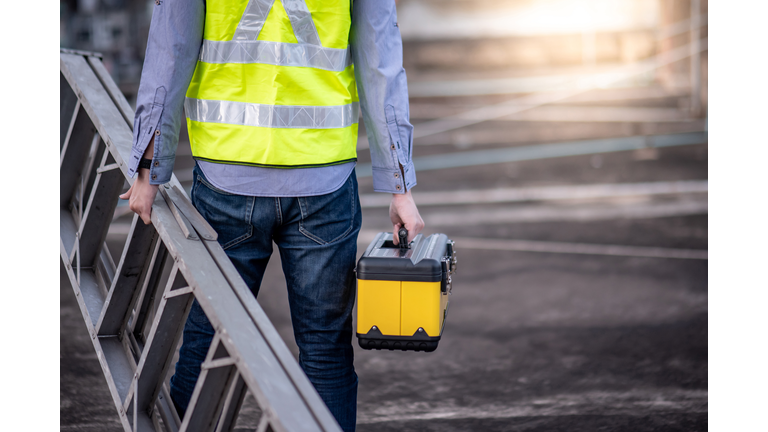 Worker man carrying aluminium ladder and tool box