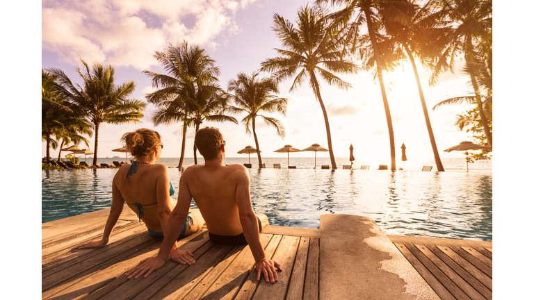 Couple enjoying beach vacation holidays at tropical resort with swimming pool and coconut palm trees near the coast with beautiful landscape at sunset, honeymoon destination