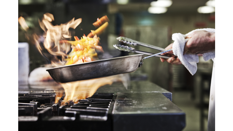 Close-up of chefs hands holding a saute pan to cook food, flambeing contents. Flames rising from the pan.