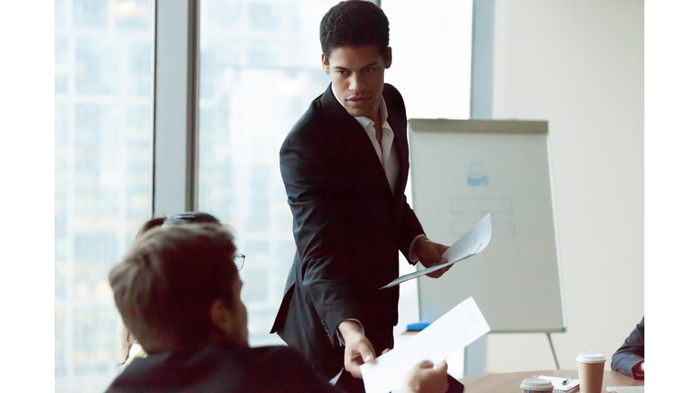 Male employee share handout material to colleagues at meeting