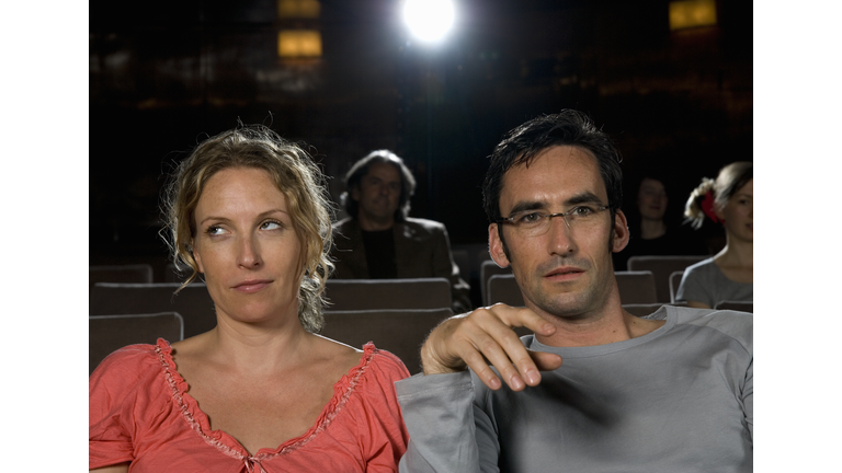 A woman rolling her eyes whilst sitting next to a man in a movie theater