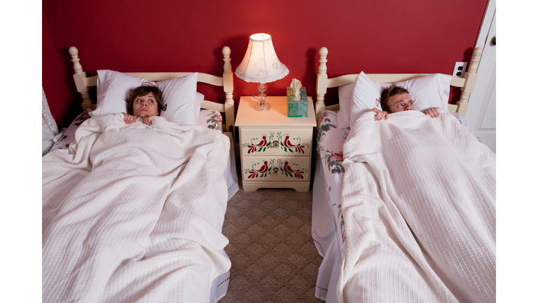 Young couple hiding under bedclothes
