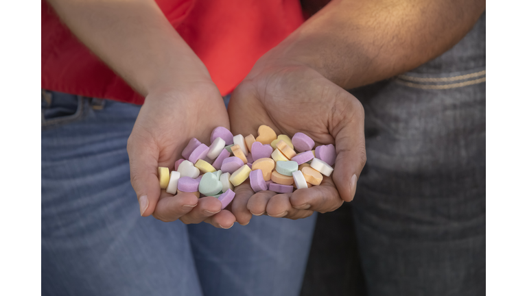 A young multiracial couple holds candy shaped hearts together on a sunny day during Valentine's day.