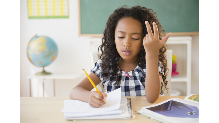 Mixed race student counting on fingers in classroom