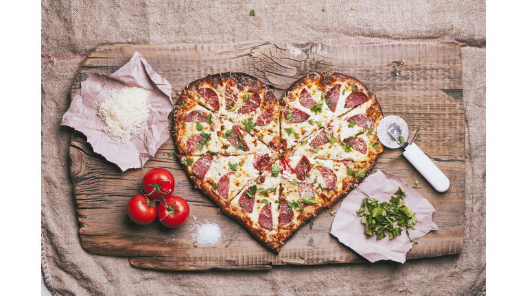 Heart-shaped pizza and ingredients on cutting board