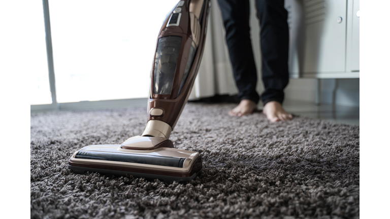 Low Section Of Man Cleaning Carpet With Vacuum Cleaner At Home