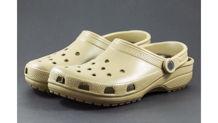 A pair of brown Crocs sandals with motif design isolated on black background.