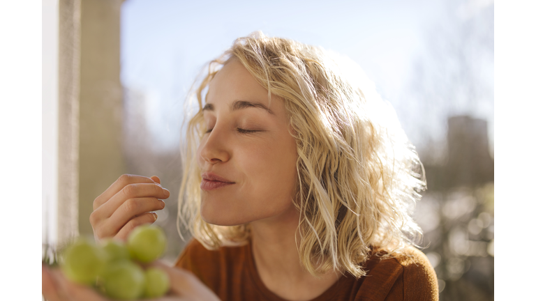 Portrait of blond young woman eating green grapes