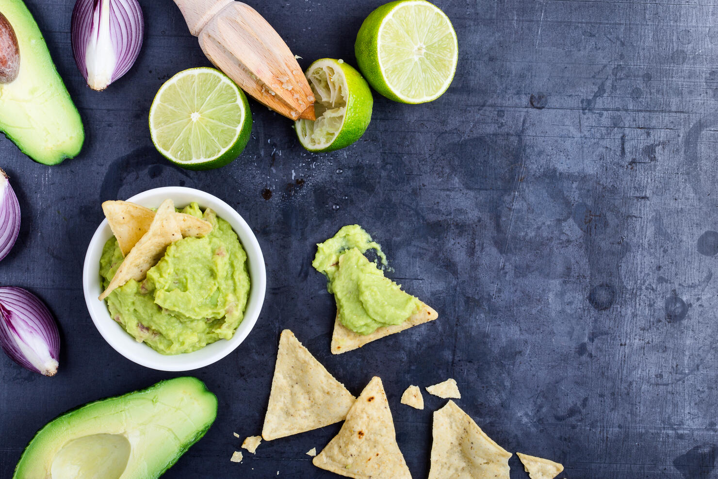 Homemade avocado guacamole dip with fresh ingredients on gark grey background with copy space