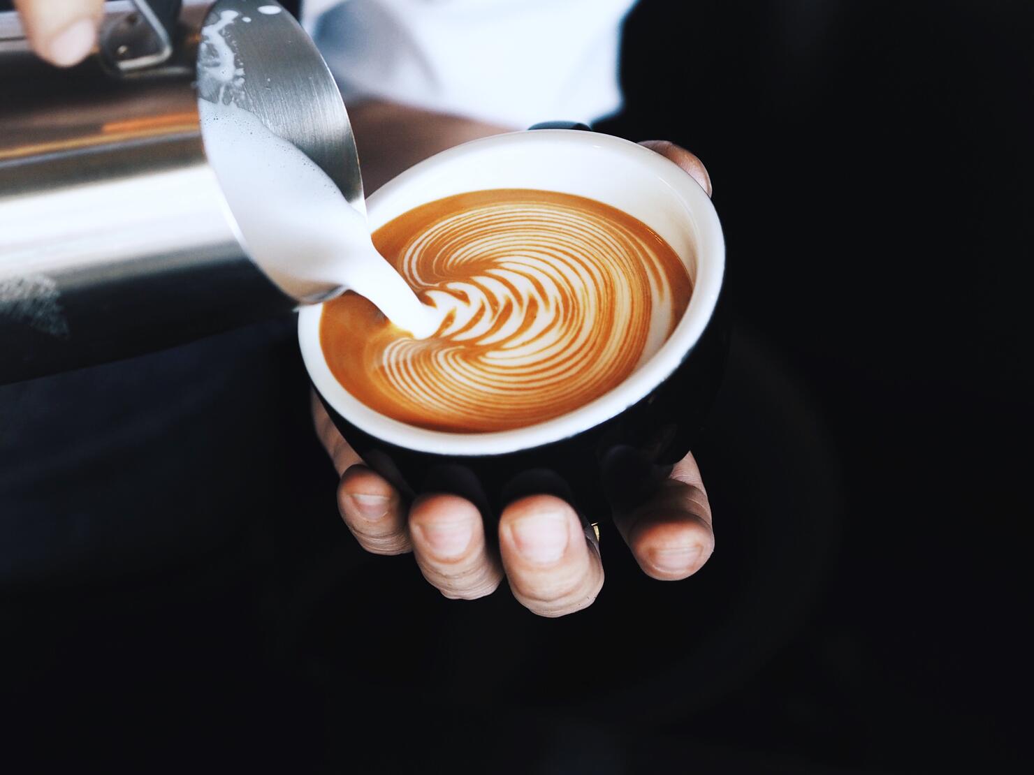 Close-Up Of Hand Pouring Milk In Coffee Cup