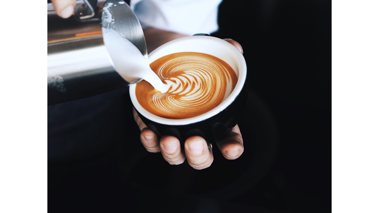 Close-Up Of Hand Pouring Milk In Coffee Cup