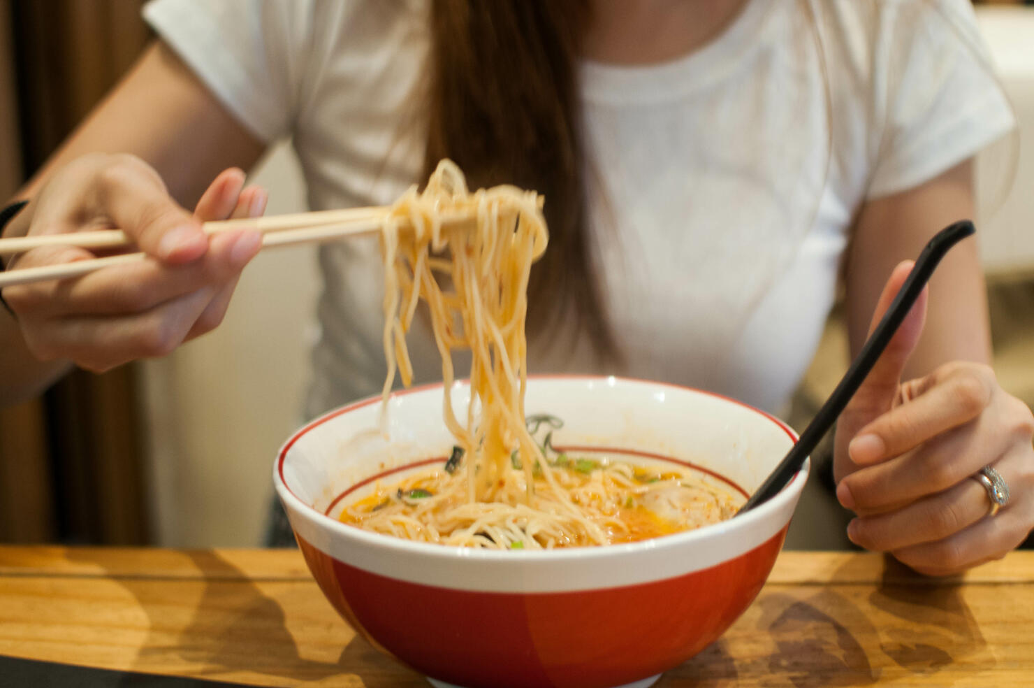 A young woman is eating a bowl of ramen on a wooden table