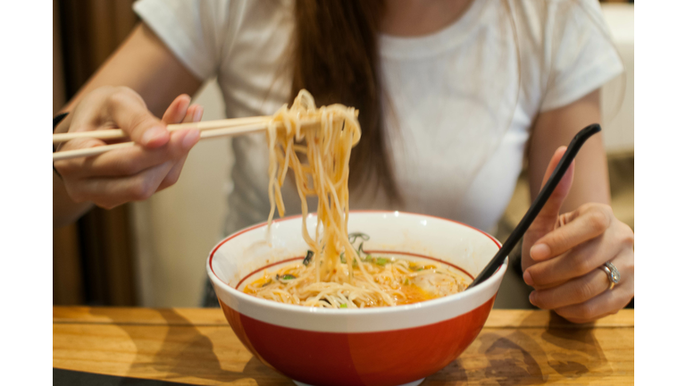 A young woman is eating a bowl of ramen on a wooden table