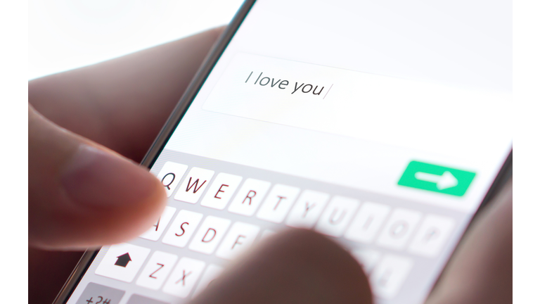 Sending I love you text message with mobile phone. Online dating, texting or catfishing concept. Romance fraud, scam or deceit with smartphone. Man writing comment.