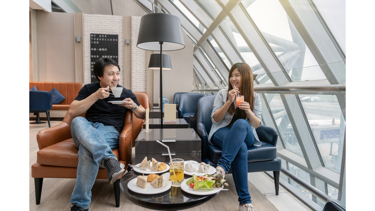 Asian couple sitting and eatting inn airport lounge when waiting the flight at modern international airport