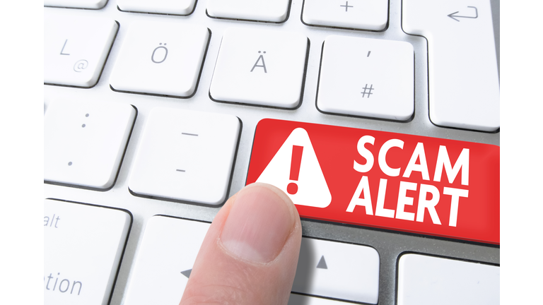 finger pressing red key labeled SCAM ALERT on computer keyboard