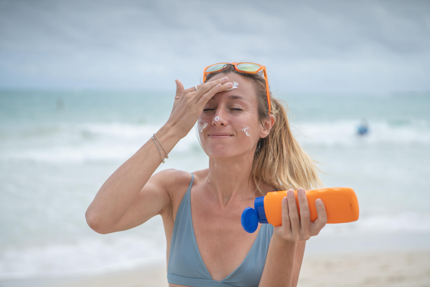 Summertime - Young woman on beach applying sunscreen on her face, protection on skin