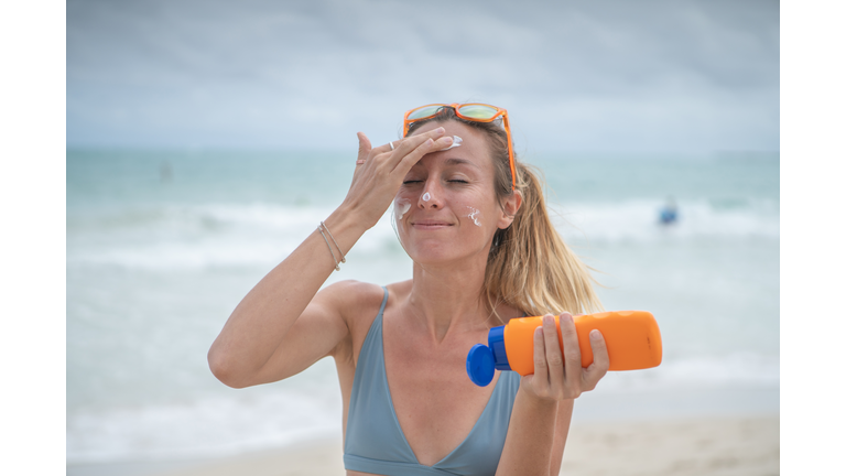 Summertime - Young woman on beach applying sunscreen on her face, protection on skin