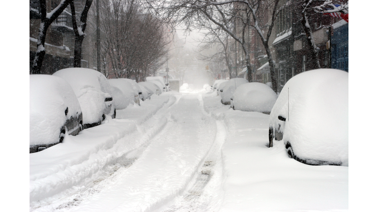 Looking down a road full of snow covered cars 