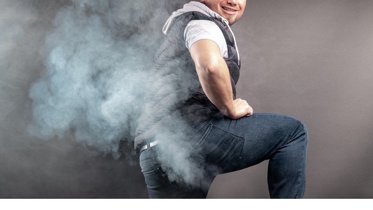 Man lift the leg and fart in front of grey background