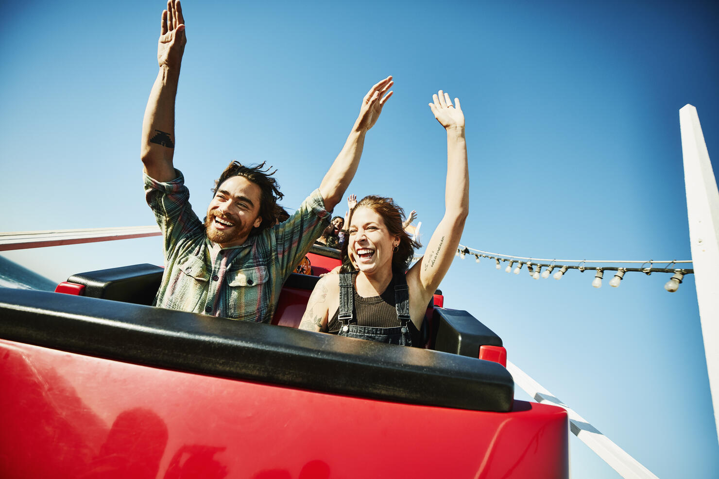 Laughing couple with arms raised riding roller coaster
