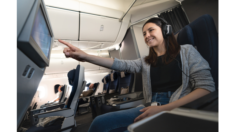 Woman traveling by plane and watching onboard entertainment