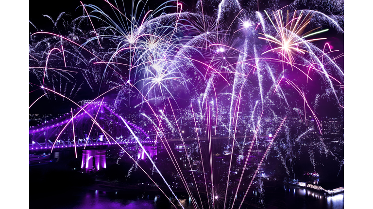 Vibrant multi colored fireworks display against the night sky with a bridge in the background