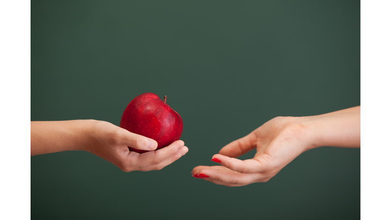 Little student hand giving red apple to teacher before blackboard