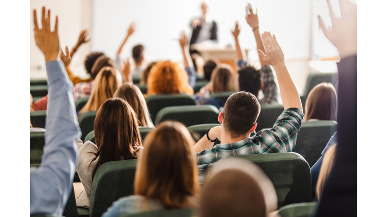 Rear view of large group of students raising arms during a class at amphitheater.