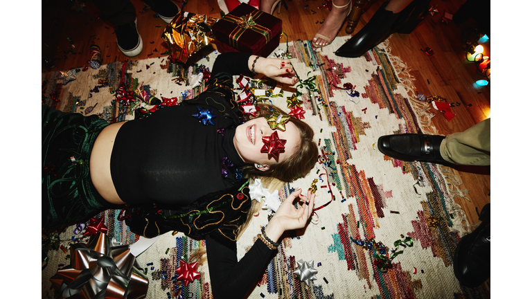 Laughing woman lying on floor with bows over eyes during holiday party with friends