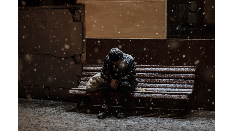 Homeless Man Sitting On Bench In Blizzard