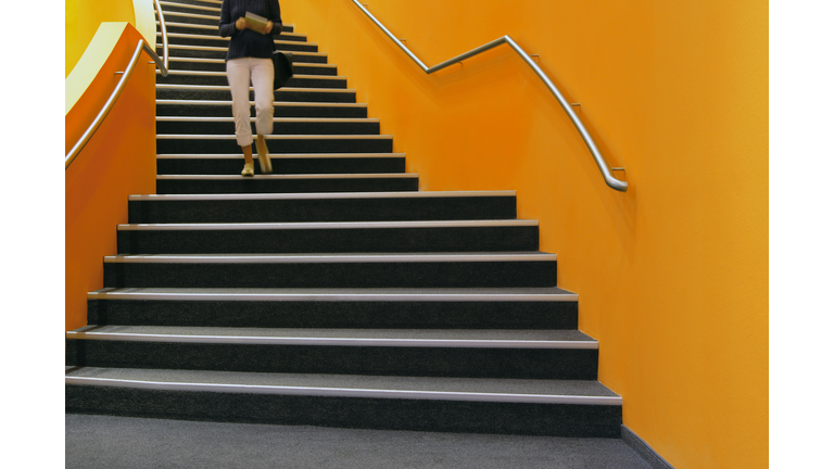 Young woman walking down orange stairs, reading book