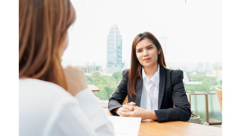 Businesswoman Taking Interview Of Woman Sitting On Desk Against Clear Sky