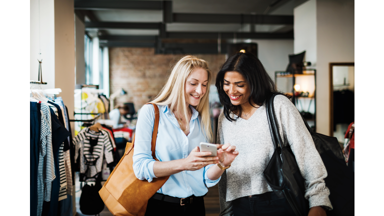 Two Womem Looking At Smartphone While Clothes Shopping