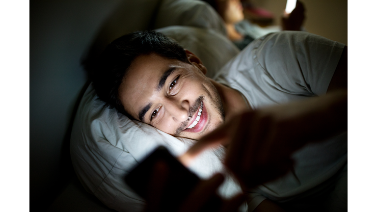 Man in bed checking his social media status on smartphone