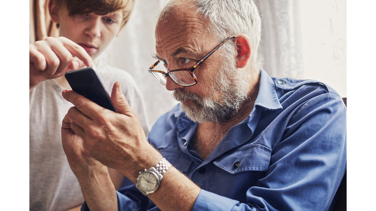 Teenager using a smartphone with his Grandfather