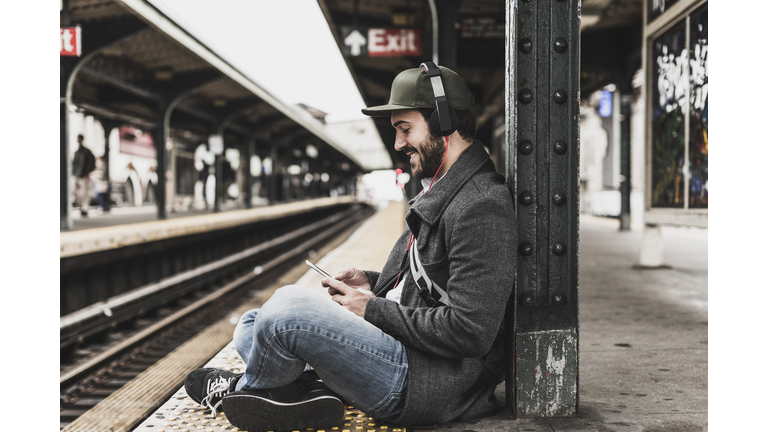 Young man waiting for metro at train station platform, using smart phone