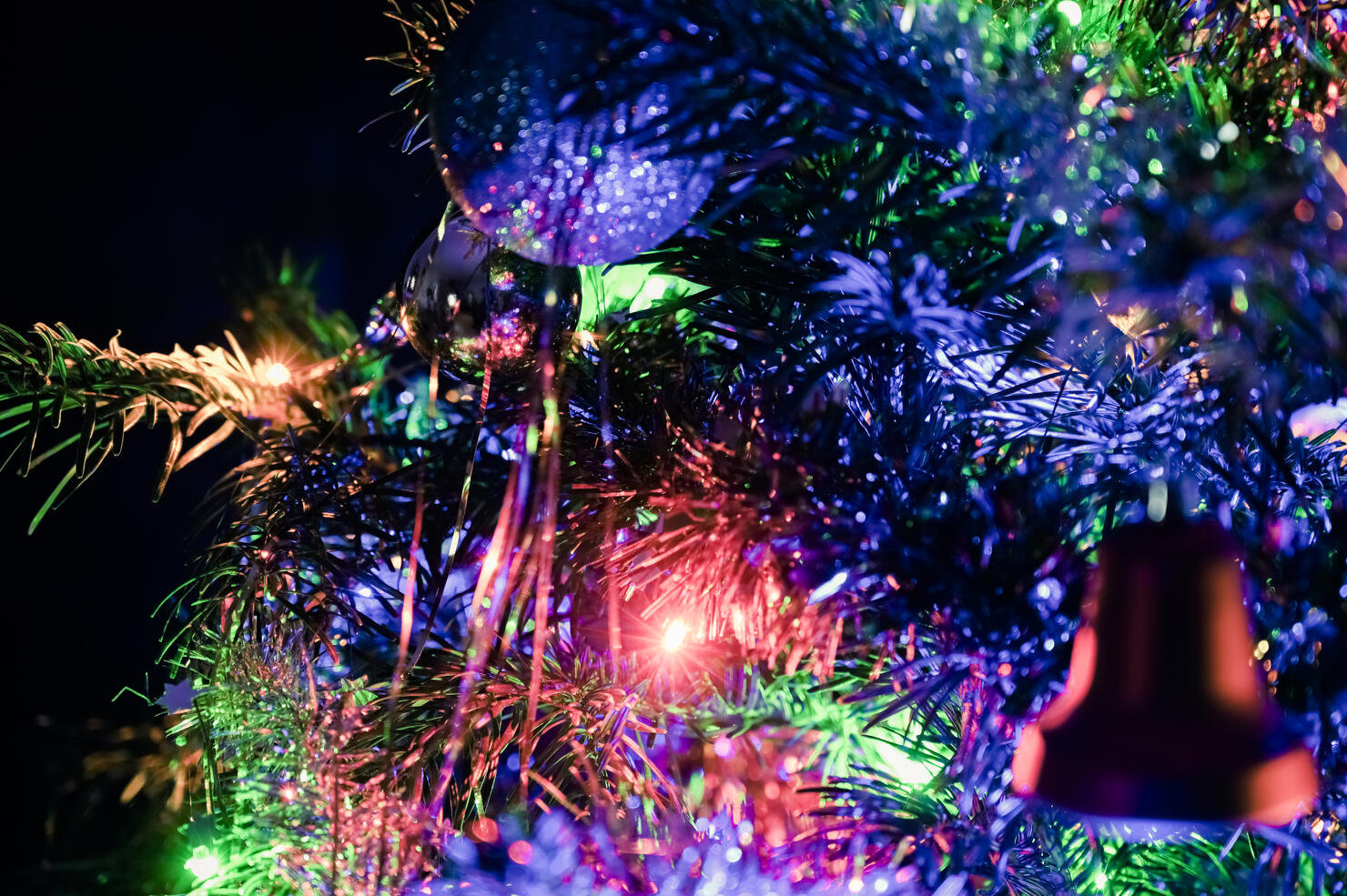 Colorful and illuminated tones of Christmas decoration of a Christmas tree. Decorated with a bell, balls, garlands and holiday lights. Black background.