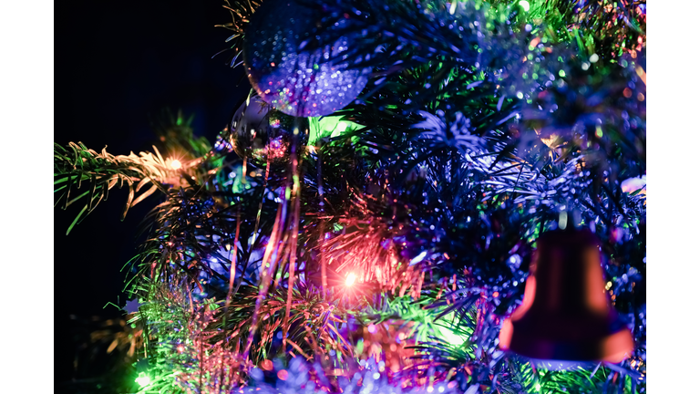 Colorful and illuminated tones of Christmas decoration of a Christmas tree. Decorated with a bell, balls, garlands and holiday lights. Black background.