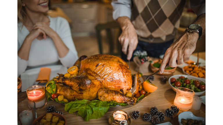 Unrecognizable person carving roasted turkey during Thanksgiving dinner at dining table.