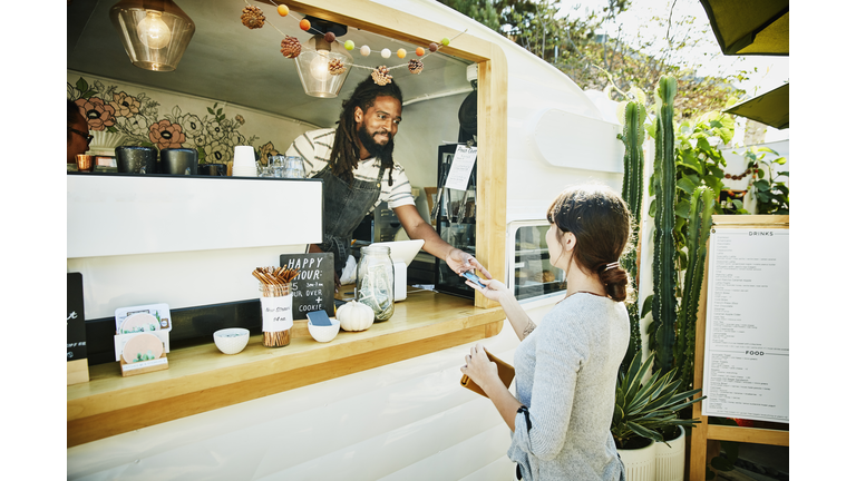 Smiling food truck owner taking credit card for payment from customer