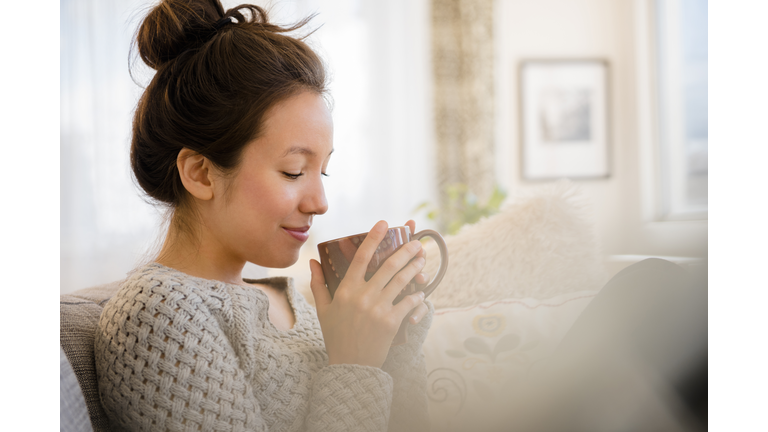 Mixed race woman drinking coffee on sofa