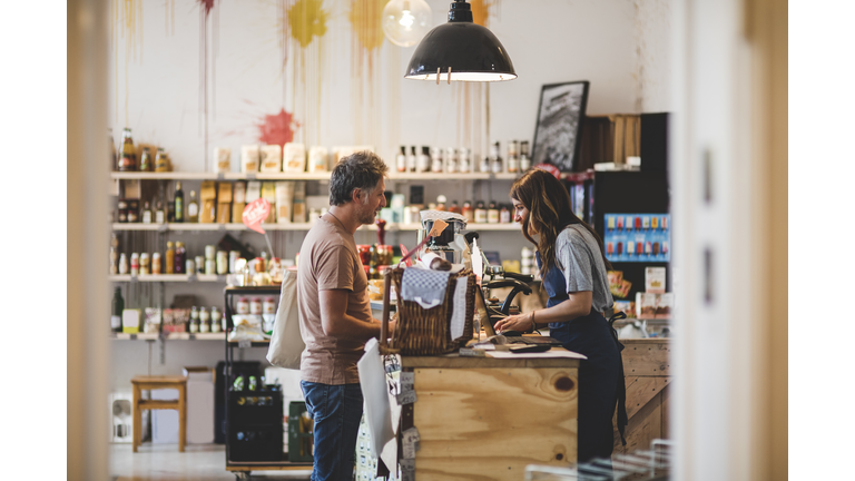 Side view of female sales clerk with customer at checkout counter in deli